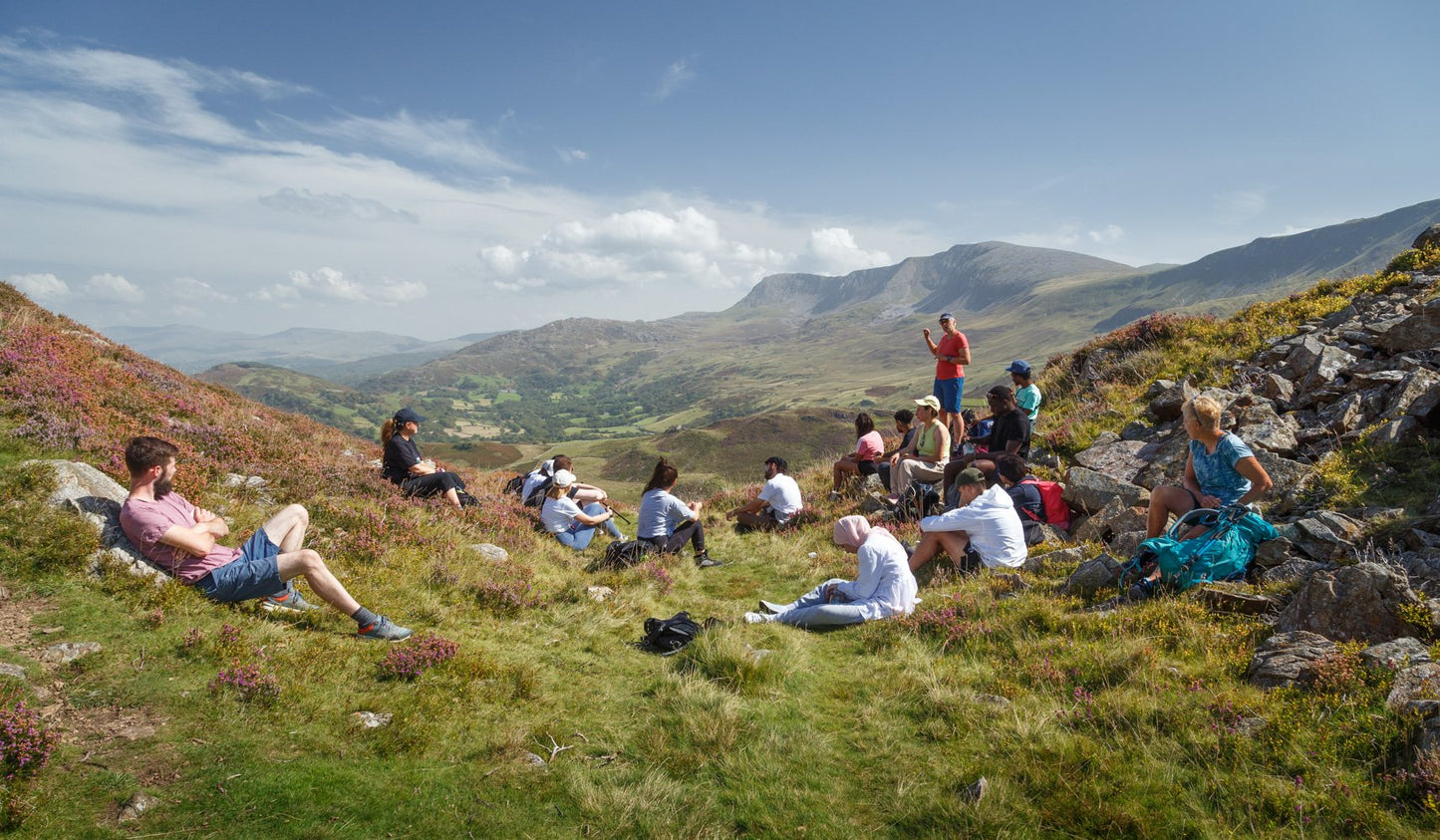 Group of hikers on mental health retreat seated on grass in welsh hills for mindfulness
