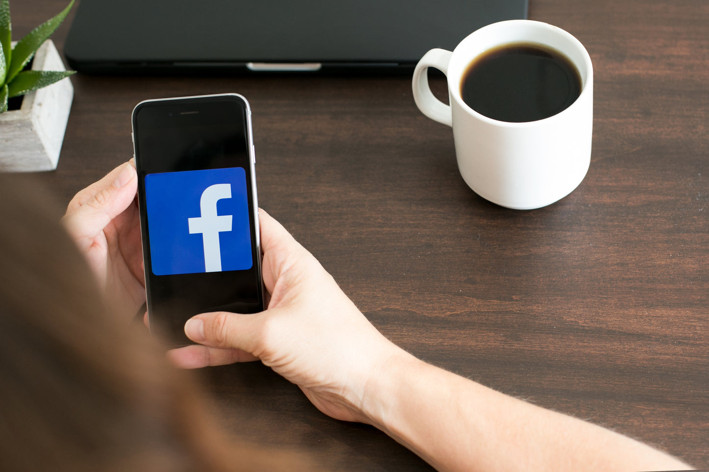 using phone to set up facebook fundraiser - hand holding phone with facebook logo and cup of coffee alongside