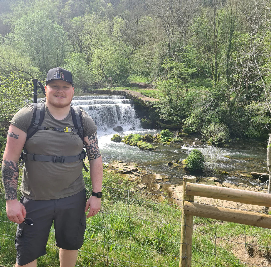 Matt standing beside a waterfall on a woodland walk, wearing hiking gear, reflecting the role of nature in supporting mental health and wellbeing.