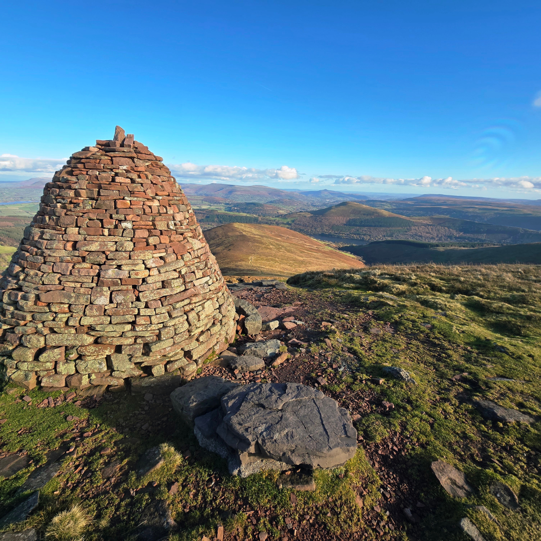 Stone cairn on a hill with a panoramic view of rolling hills and blue sky.