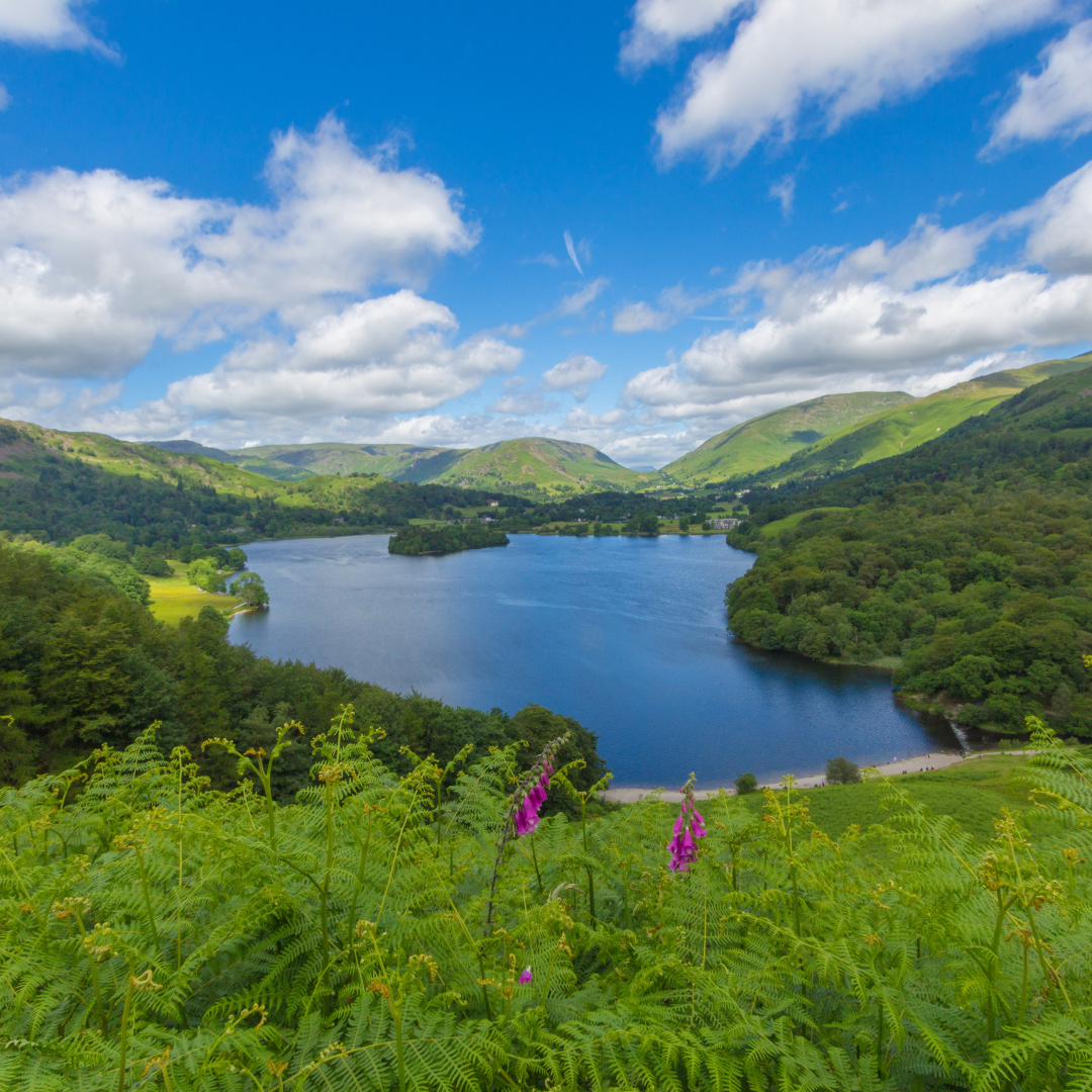 Lake surrounded by green hills and blue sky with clouds