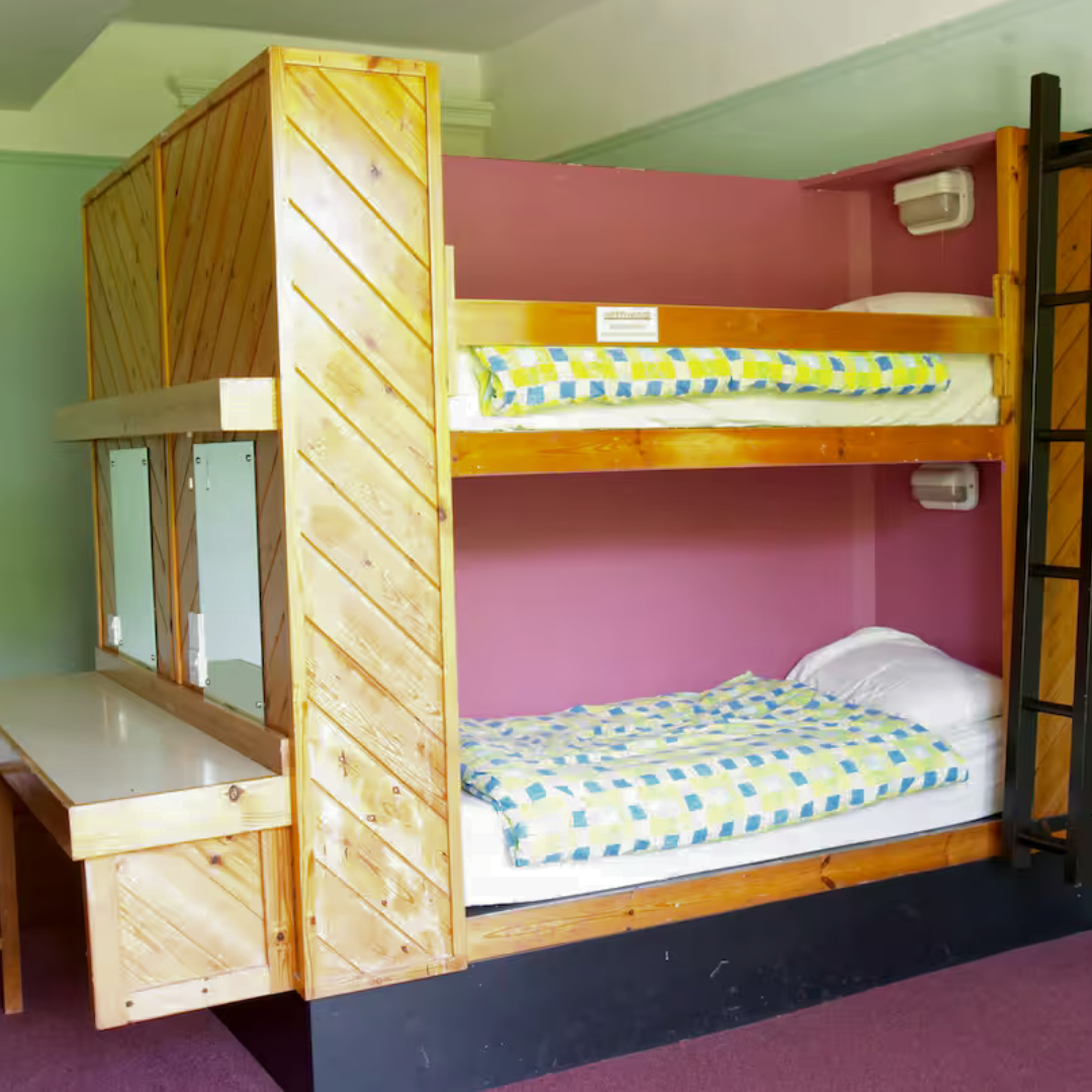 Wooden bunk bed with a desk in a room with pink walls.
