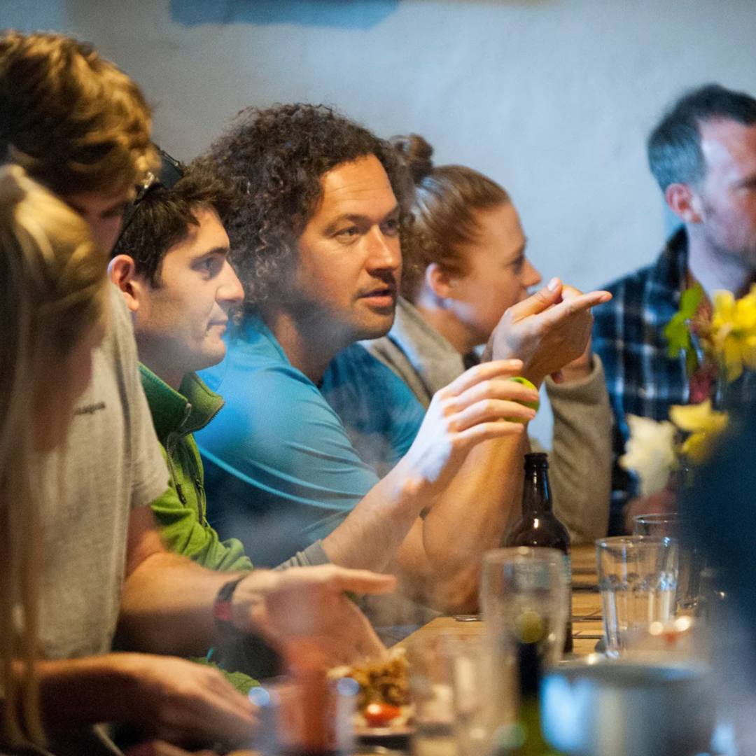 Group of people sitting around a table with drinks and food, engaged in conversation.