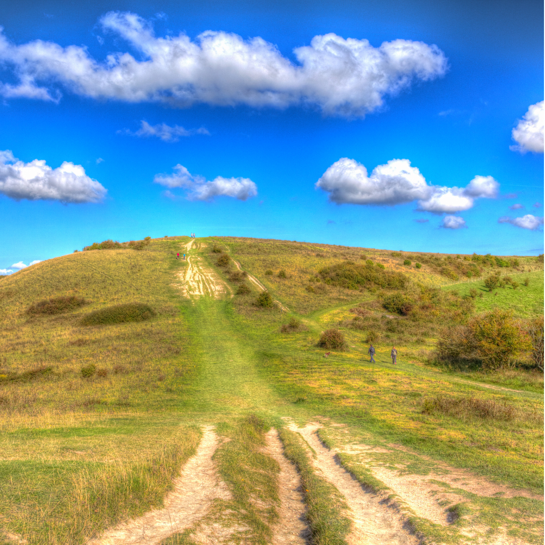 Hilly landscape with a dirt path under a blue sky with clouds