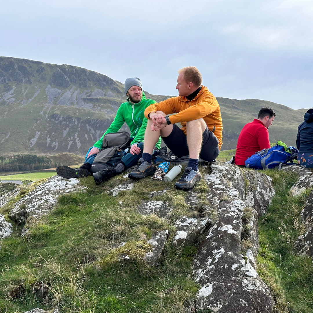 Two men sitting on a rocky outcrop with mountains in the background