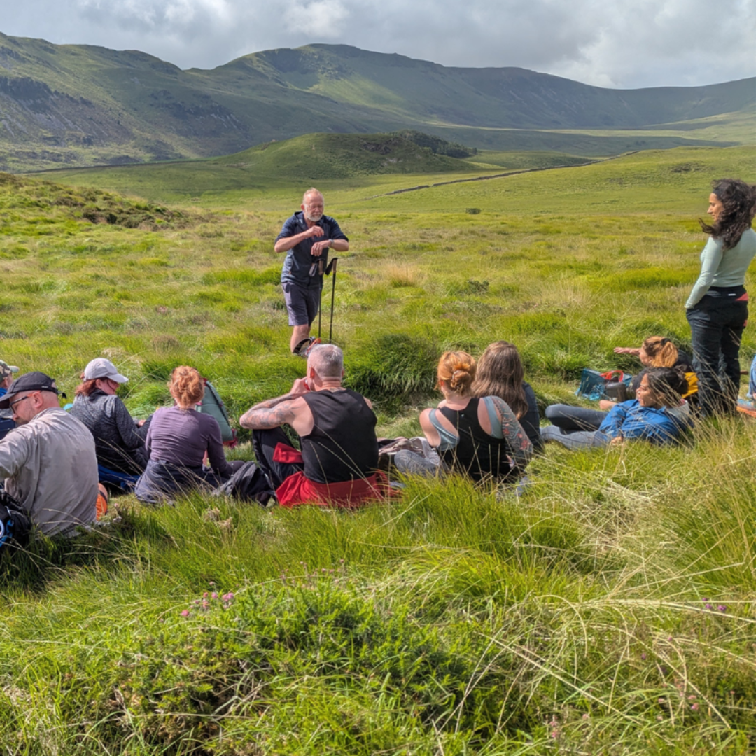 Group of people sitting in a grassy field with mountains in the background