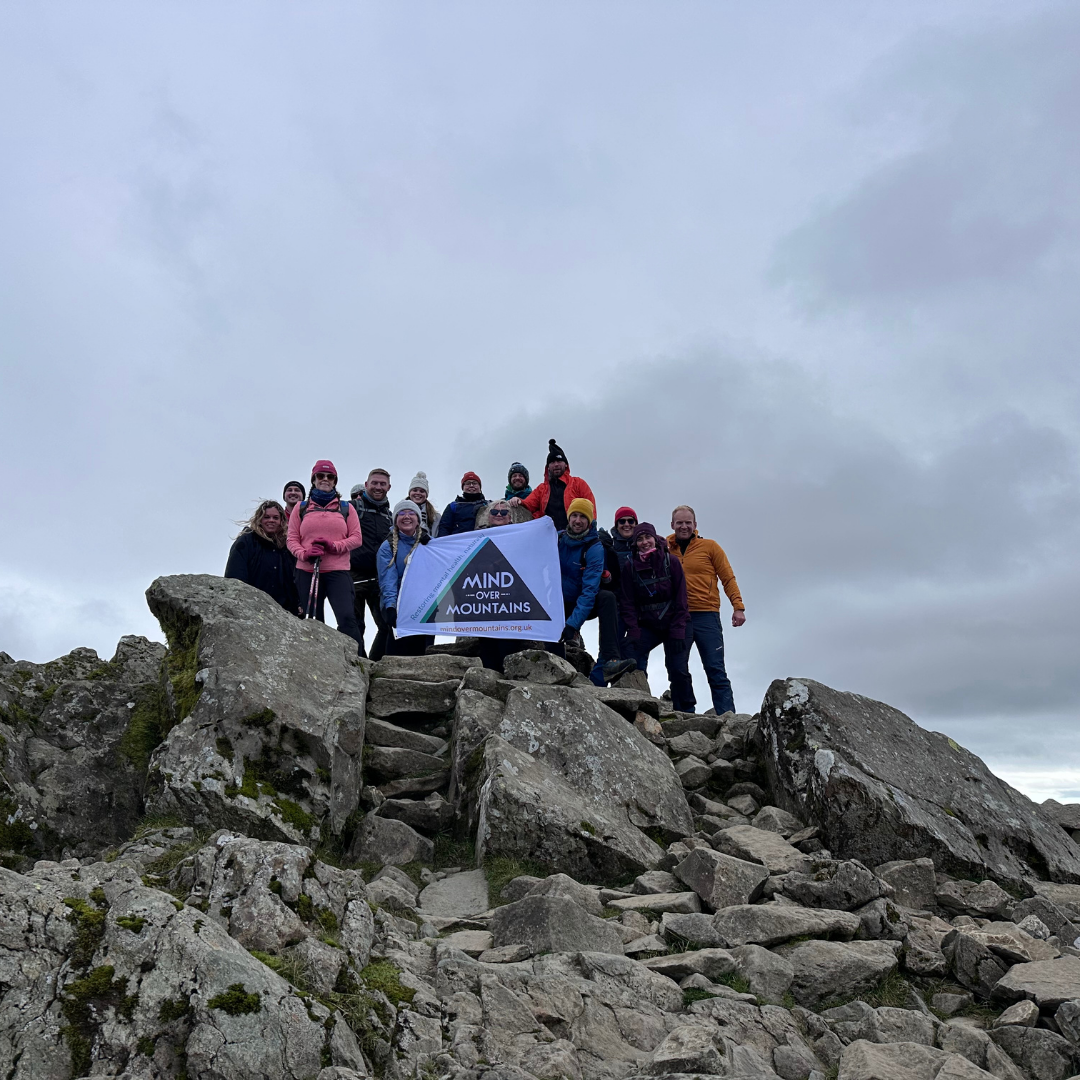 Group of people standing on a rocky mountain top with a banner.