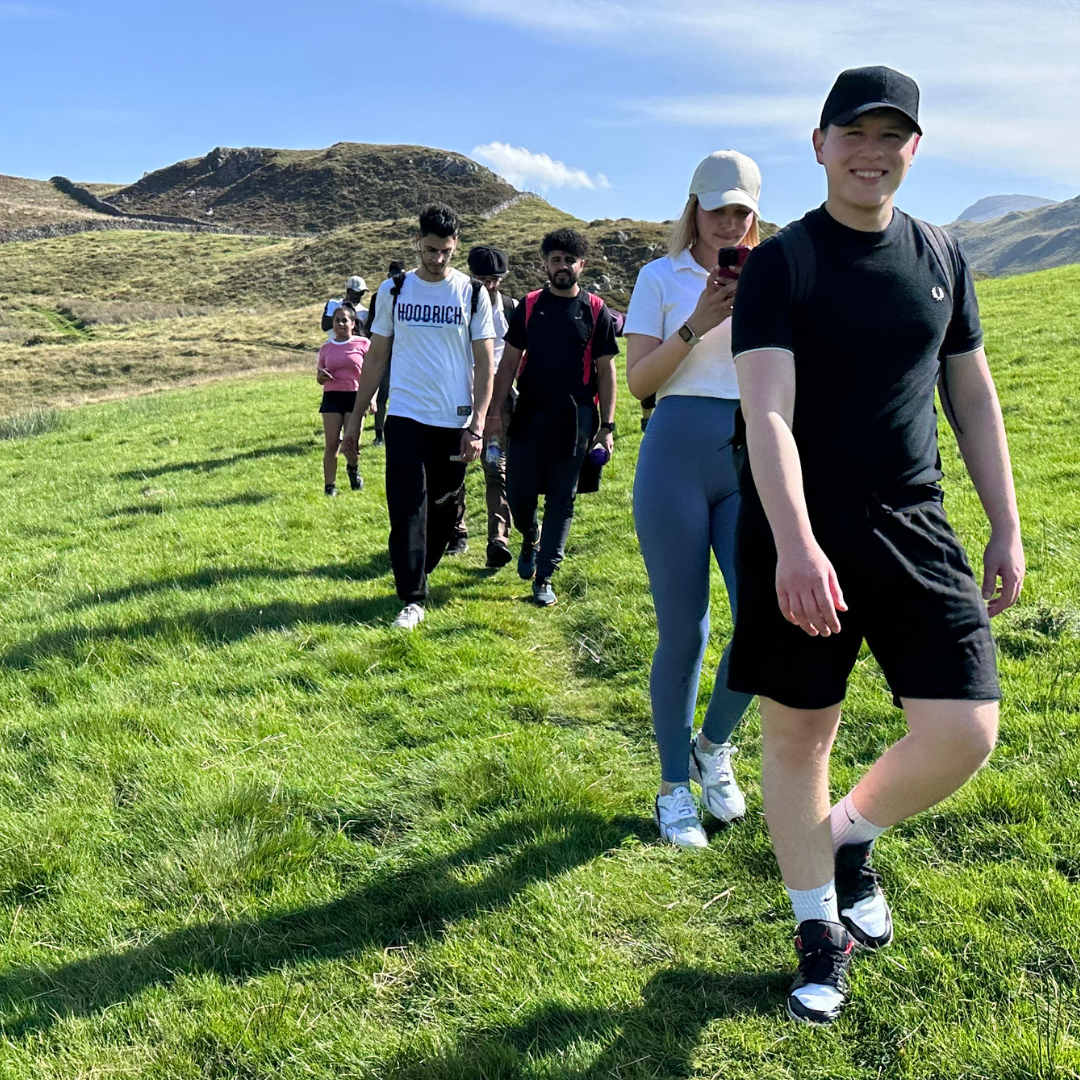 Group of people walking on a grassy hill with mountains in the background