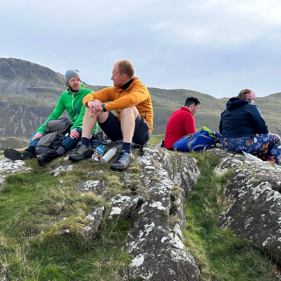 Group of people sitting on a rocky outcrop with mountains in the background