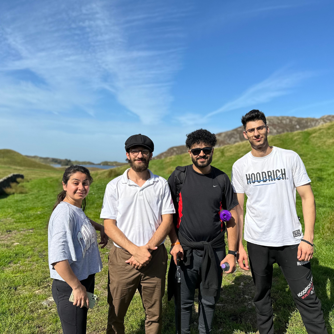 Four people standing in a grassy field with a clear blue sky.