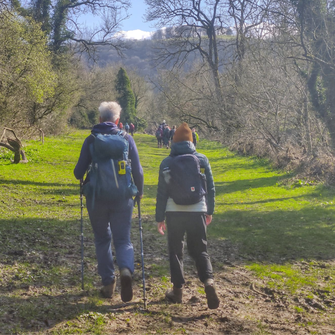 Two hikers walking on a trail with mountains in the background