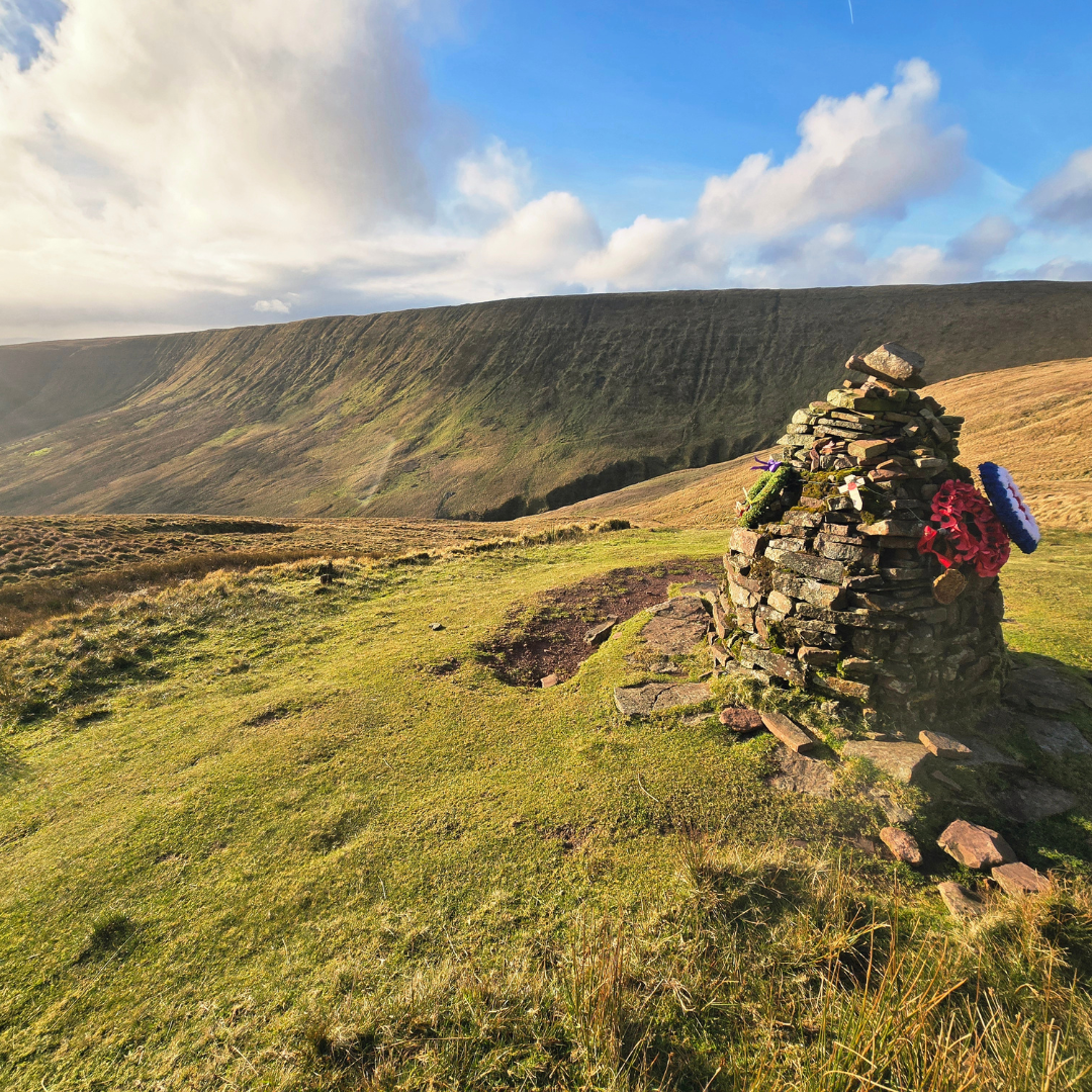 Stone cairn on a grassy hill with a scenic landscape and blue sky.