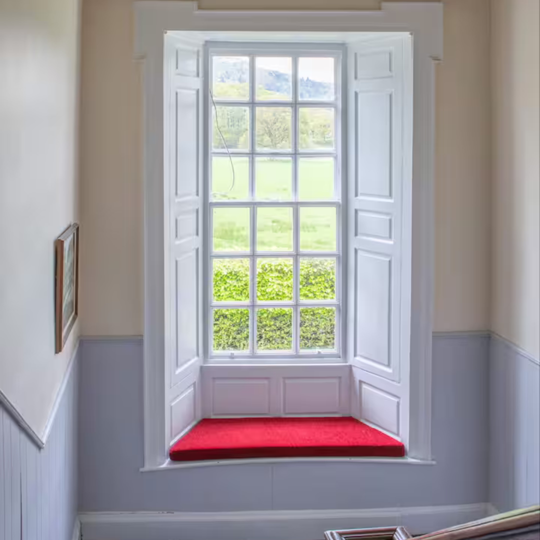 Window seat with a red cushion in a room with white walls and a framed picture.