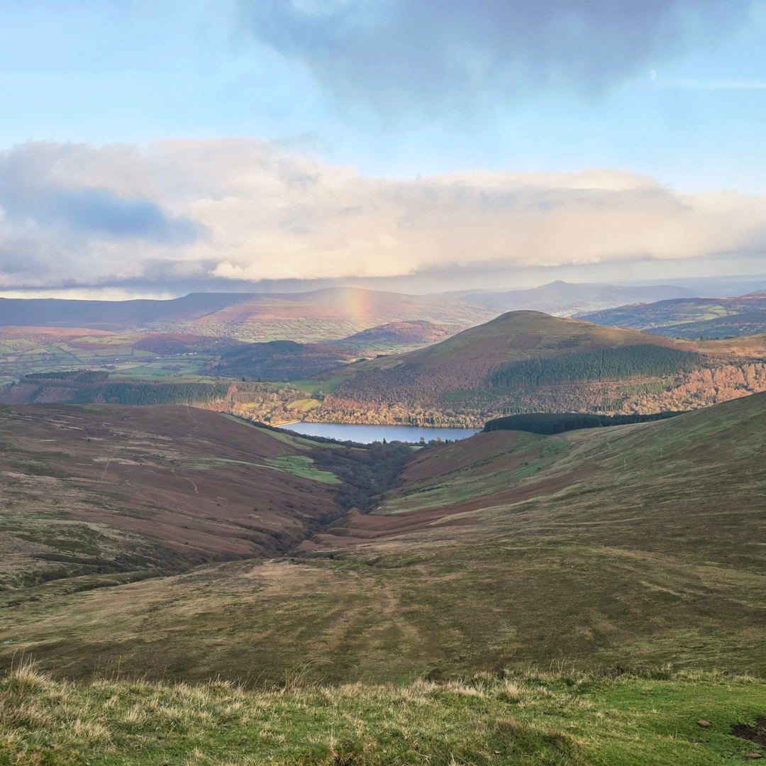 Scenic view of a valley with hills and a rainbow in the distance