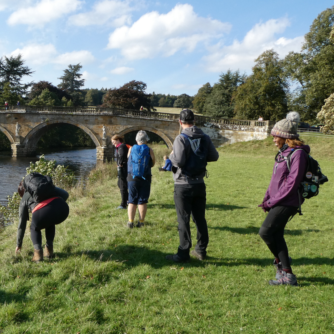 hikers along riverside in front of bridge