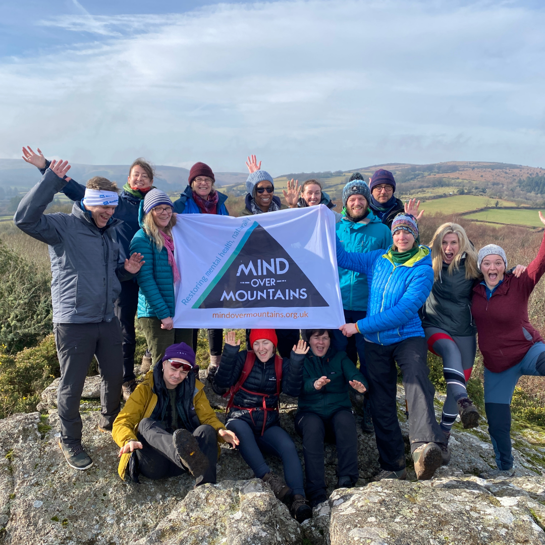 Mind Over Mountains hiking group on mental health retreat with flag on top of stone tor