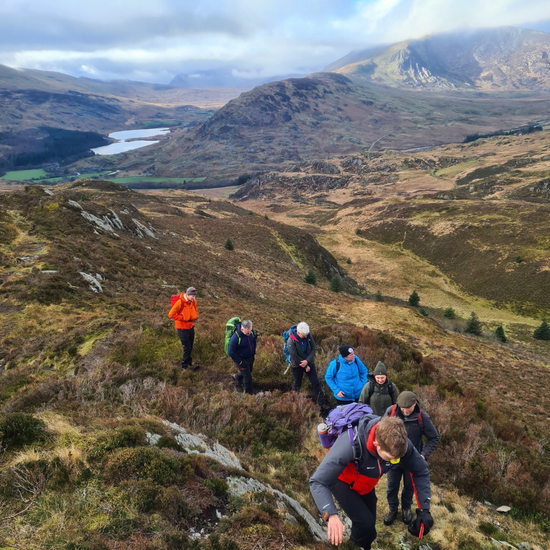Lake District hiking group coming uphill with mountains beyond during wellbeing retreat with charity Mind Over Mountains supporting mental health