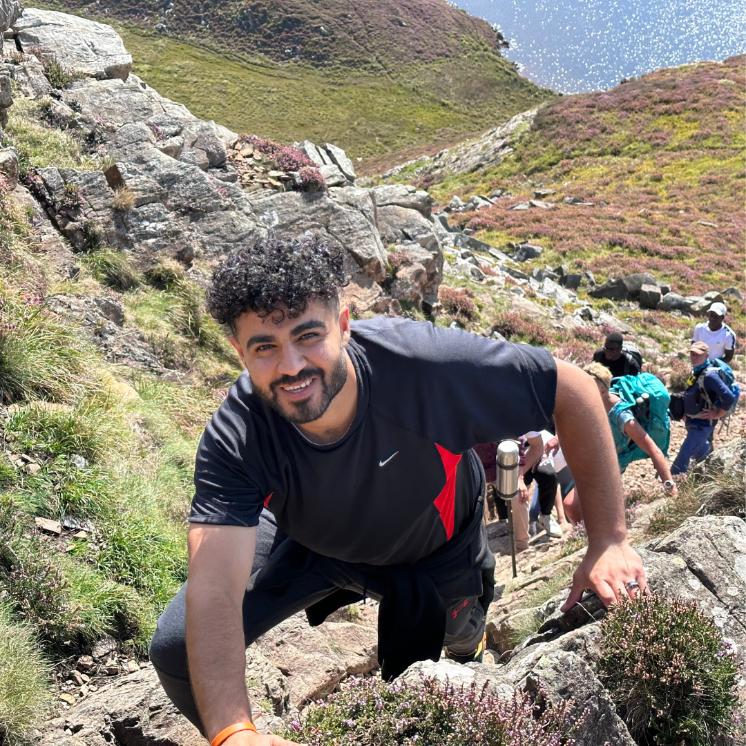 man climbing rocky path with group of hikers with charity Mind Over Mountains - above coastline in Wales