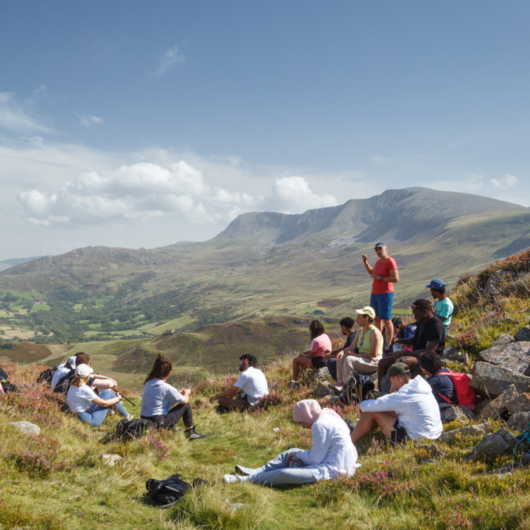 group of hikers listening to wellbeing coach in mountains