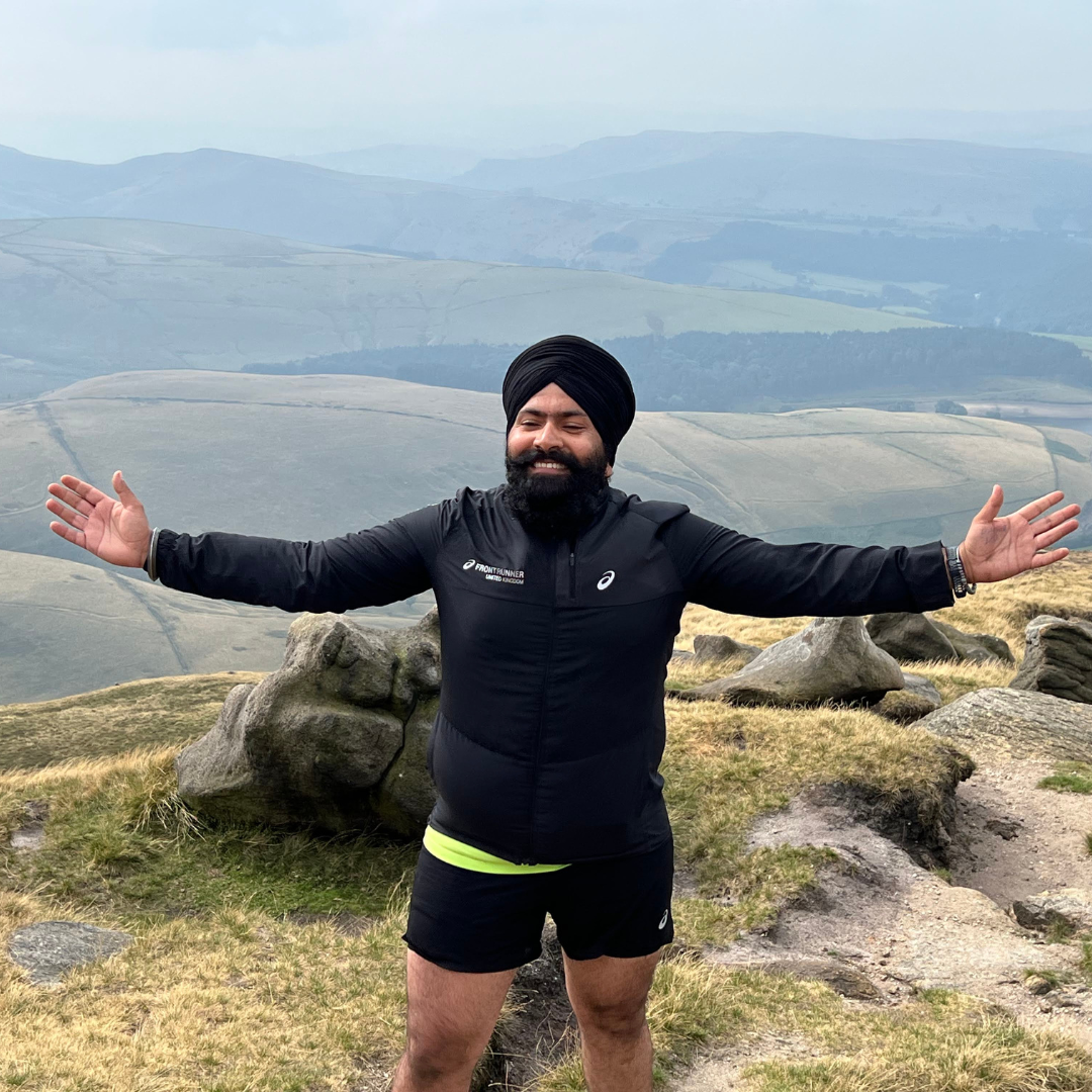 sikh man hiking for mental wellbeing in mountains arms spread at summit